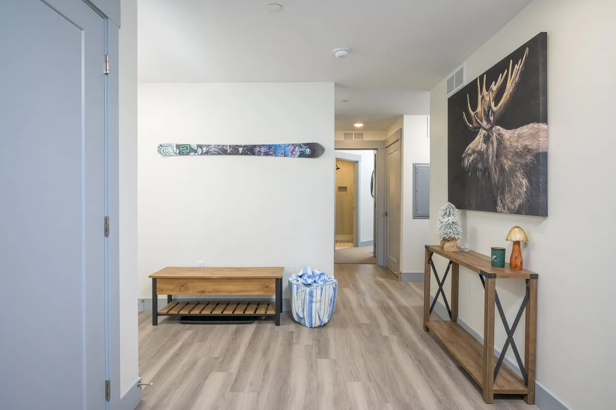 A welcoming entryway with a ski board mounted on the wall, moose artwork, a wooden bench, and a decorative console table. The space is casual and inviting, suggesting a transition from outdoor adventure to cozy indoor relaxation.