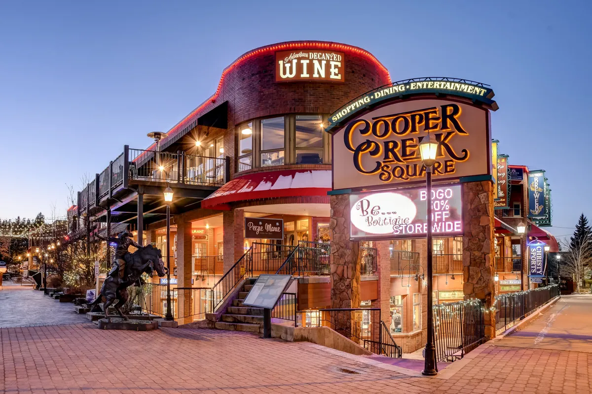 An exterior shot of Cooper Creek Square, featuring decorative lights, a wine shop, staircase, and an inviting plaza setting. The image evokes the festive and lively spirit of downtown, with opportunities for shopping, dining, and entertainment just steps away.