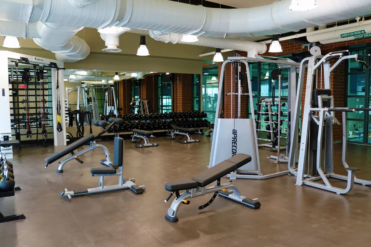 A modern, well-equipped gym interior featuring mirrored walls, weightlifting equipment, and cardio machines. The space is clean, organized, and motivational, reflecting the high-quality fitness facilities of the Grand Park Rec Center.