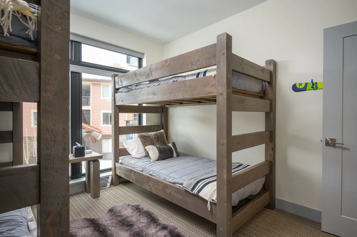 A playful and relaxed bunk bedroom setup with twin-over-twin bunk beds, a textured rug, and large windows. The environment feels youthful and fun, inviting both sleep and play.