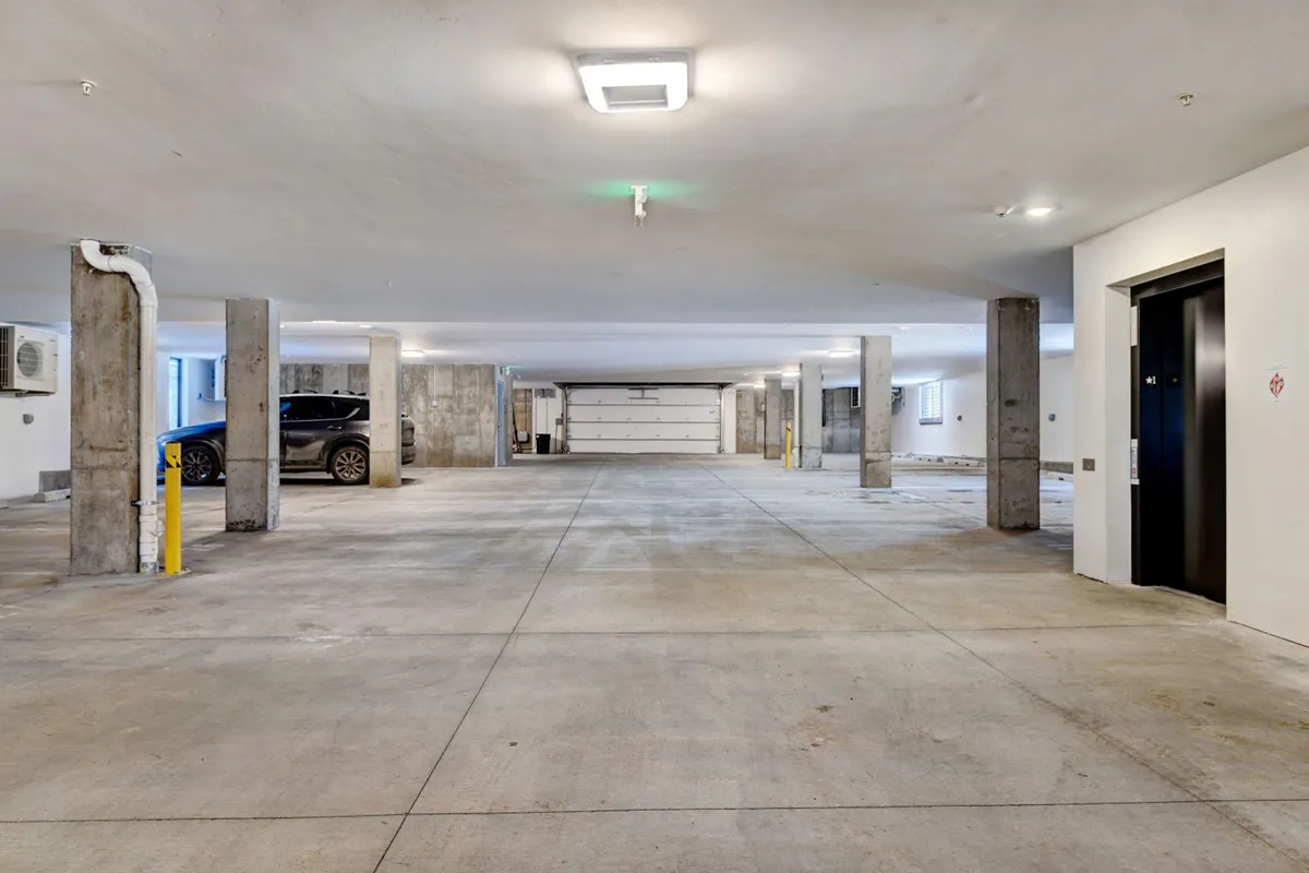 An interior view of the heated underground garage, showing marked parking spaces, an elevator entrance, and support columns. The space is functional and modern, emphasizing convenience and comfort for guests arriving in any season.
