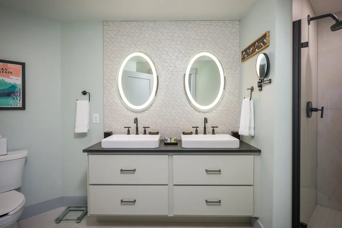 A modern, inviting bathroom with double sinks, elegant oval mirrors with LED backlighting, and a geometric patterned accent wall. The atmosphere is refreshing and ideal for self-care.