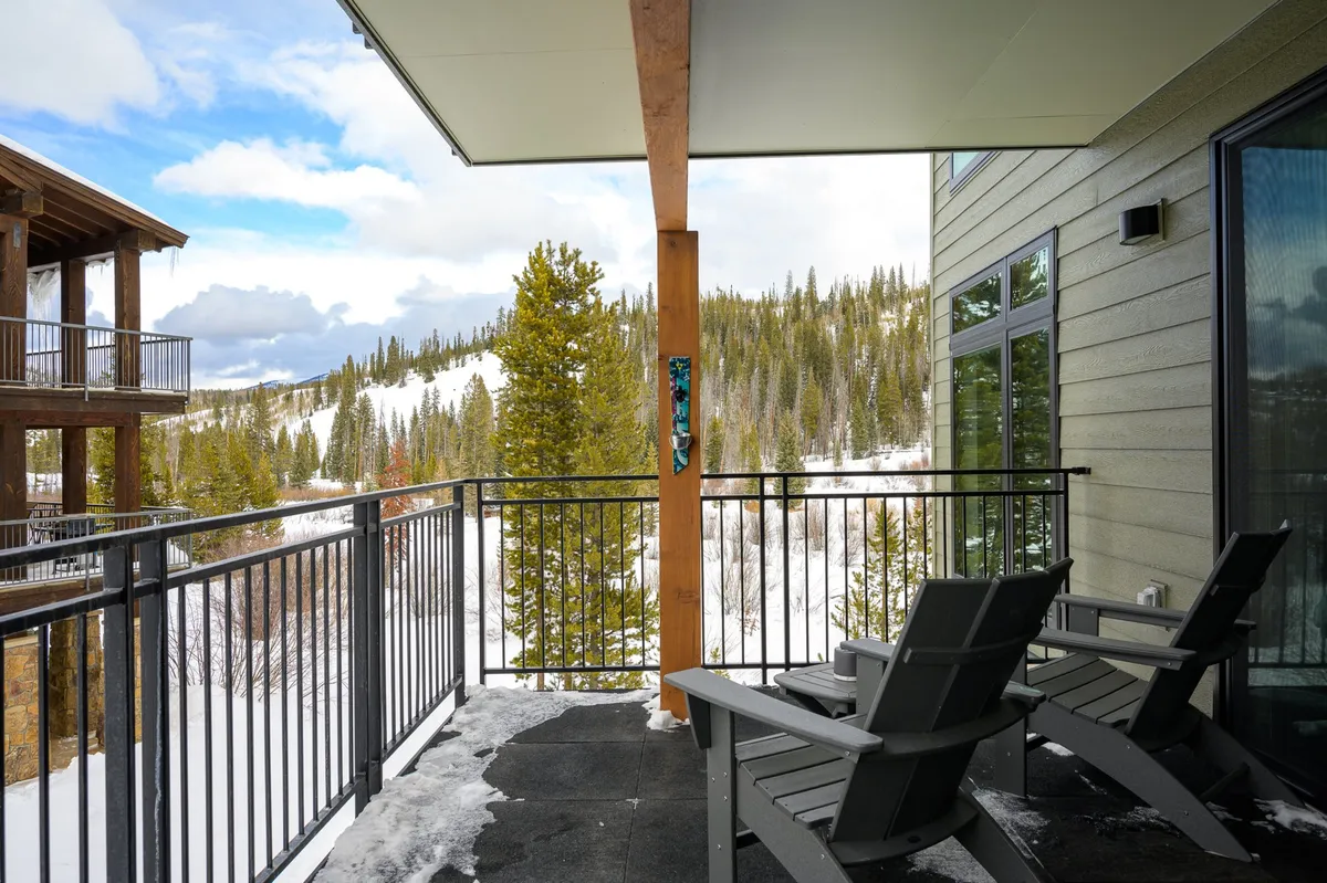 A private balcony with comfortable seating overlooks snow-covered trees and mountain vistas. The scene is peaceful, offering opportunities to spot wildlife, listen to concerts, or simply enjoy the tranquility of nature.