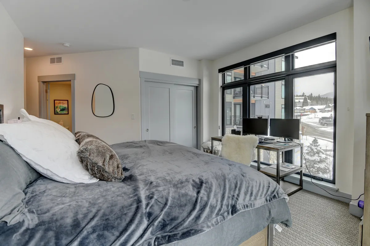 This image showcases a serene bedroom featuring a comfortable bed, large windows that bathe the space in natural light, and a work desk. The design is minimal yet inviting, evoking a sense of relaxation and privacy.