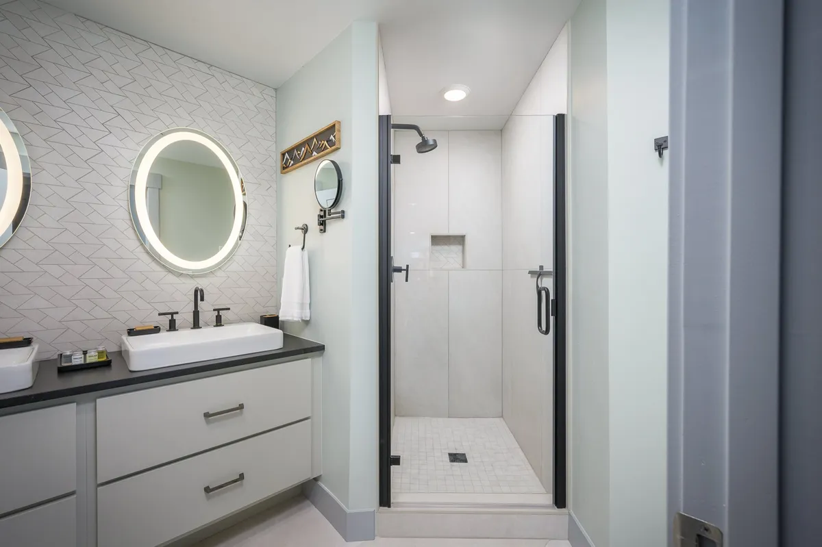 A bright, modern bathroom with dual circular mirrors, elegant sinks, and a glass-enclosed shower. The space feels fresh, clean, and inviting, communicating a sense of careful maintenance and attention to hygiene.